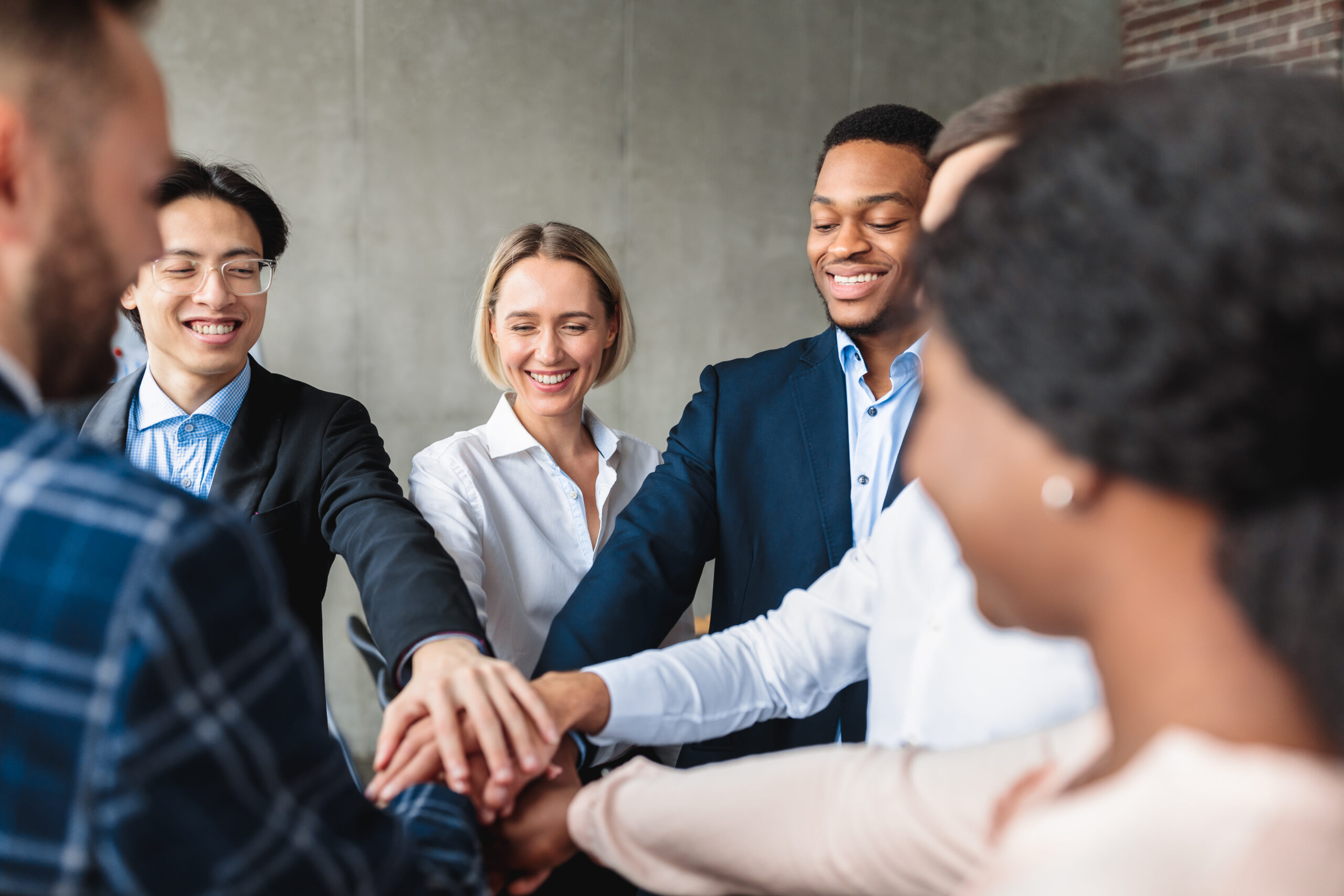 A multiracial team of business professionals joining hands in an office setting.