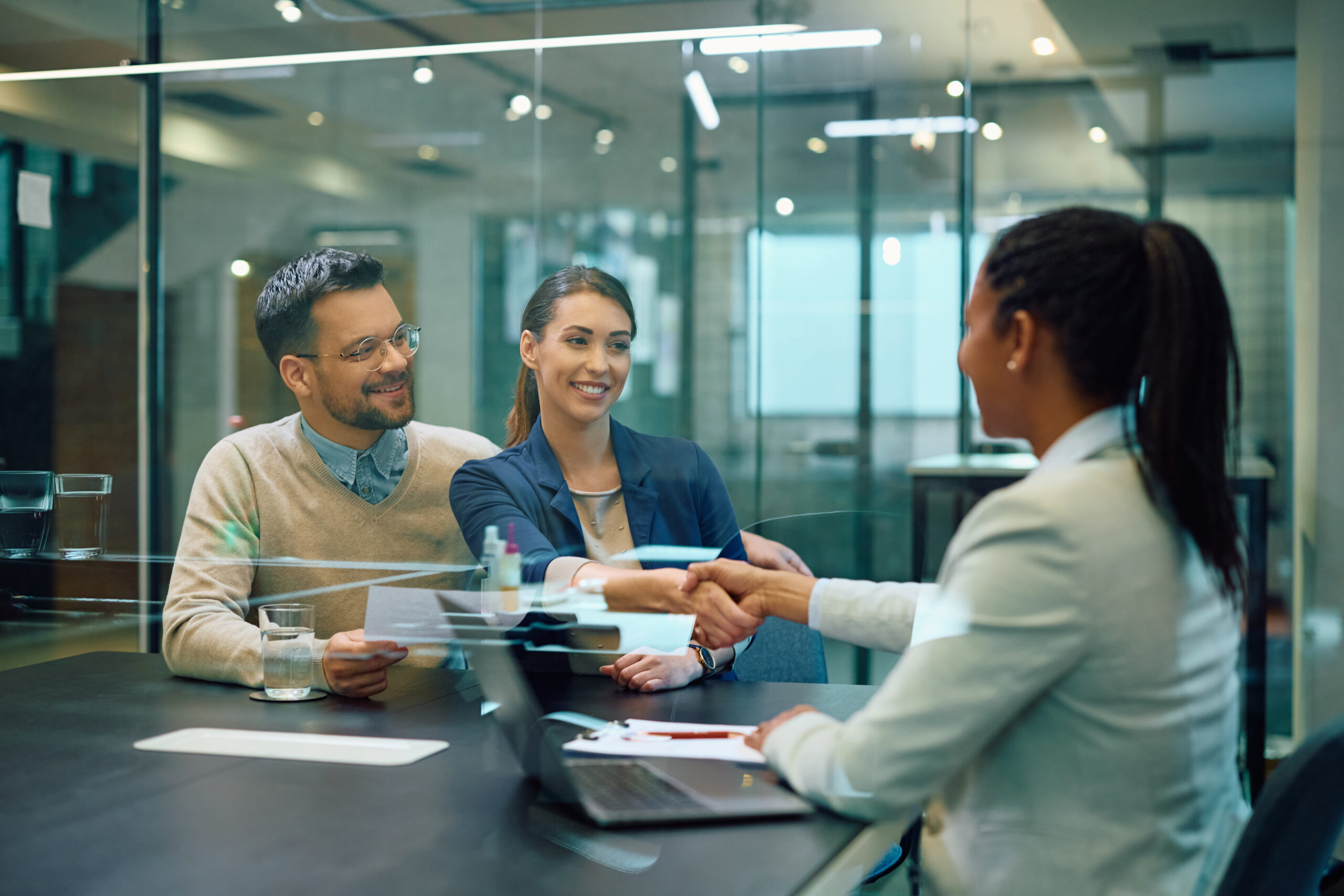 A happy couple shaking hands with a sales representative after a closed deal.